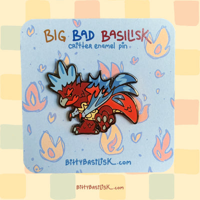 An enamel pin featuring a stylized basilisk with blue and red coloring on a card with flame designs.